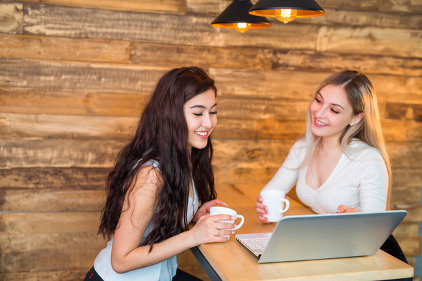 two beautiful young women are sitting at a table with a laptop - Photo, Image