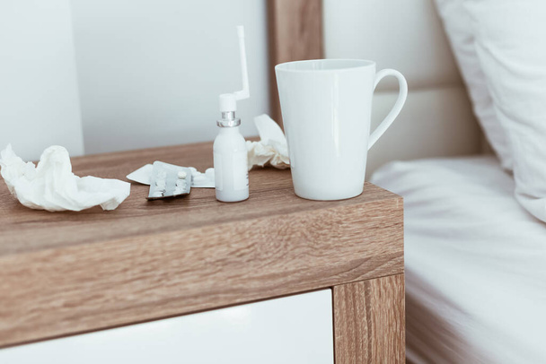 Medicines, pills, nose drops, tissues and hot drink cup on bedside table in modern apartments. Being sick, unwell, flu, illness symptoms. Coronavirus home treatment concept. Lifestyle image copy space - Foto, immagini