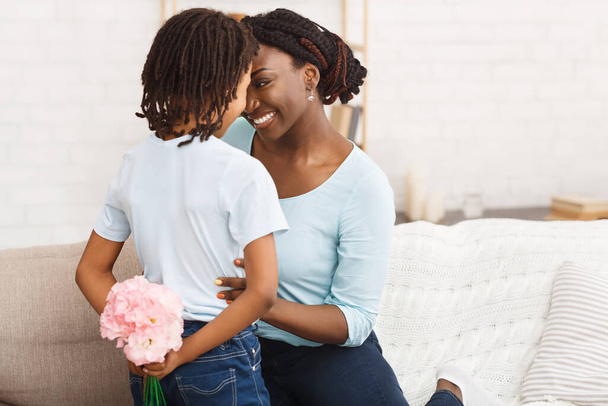 Afro girl congratulating her mom with flowers on couch - 写真・画像