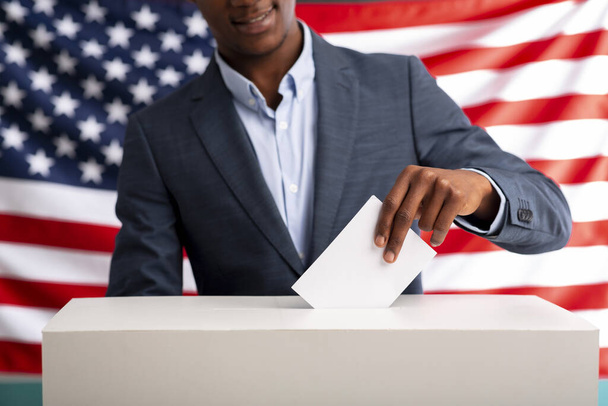 Счастливый африканский американец голосует, вставляя бумагу в урну для голосования
 - Фото, изображение