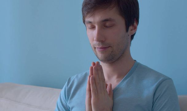 Porträt eines meditierenden jungen Mannes auf blauem Hintergrund. Aus nächster Nähe. Das Konzept von Meditation, Entspannung, Yoga, Stressabbau und innerer Ruhe - Foto, Bild
