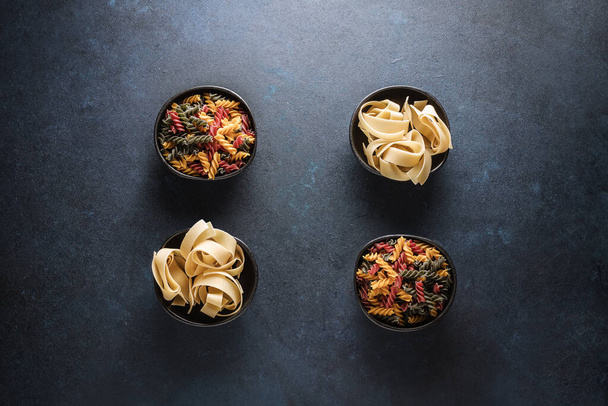 4 bols de pâte crue type boucles colorées et nouilles pâtes sur une table rustique. Concept de cuisine italienne traditionnelle.Style Moody
 - Photo, image