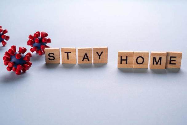 Stay home stay safe concept made up of wooden letters and models of covid-19 virus on blue background - Foto, Imagem