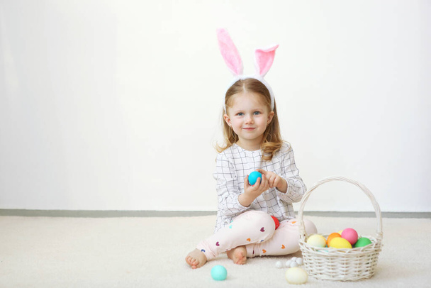 Aranyos kislány húsvéti kosárral, könnyű háttérrel. Helyezze be a szöveget. Húsvéti hagyományok. Boldog húsvétot!! - Fotó, kép