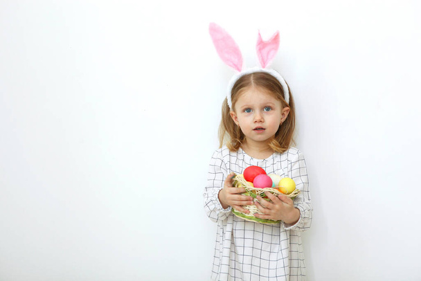 Aranyos kislány húsvéti kosárral, könnyű háttérrel. Helyezze be a szöveget. Húsvéti hagyományok. Boldog húsvétot!! - Fotó, kép