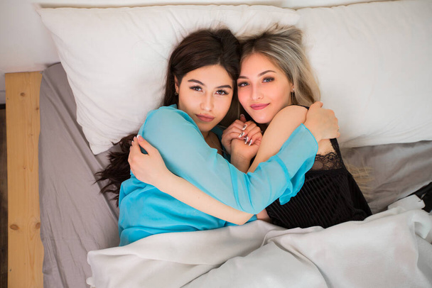 İki güzel genç kadın yatak odasında yatağın üstünde. - Fotoğraf, Görsel