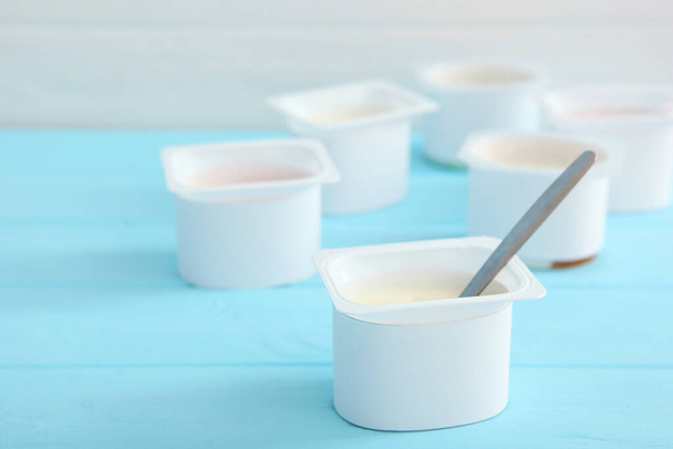 Leckerer Joghurt in einem Plastikglas auf einer farbigen Tischplatte. Platz zum Einfügen von Text. Nützlicher Imbiss. - Foto, Bild