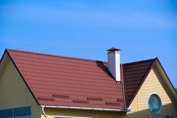 techo y chimenea de la pequeña casa - láminas de techo de perfil rojo de acero, pared de revestimiento amarillo y cielo azul
 - Foto, Imagen
