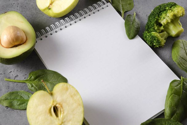 Apple, half  avocado halves with a stone,  broccoli, fresh green spinach leaves, a blank sheet of Notepad on a gray background,  copy space - Photo, image