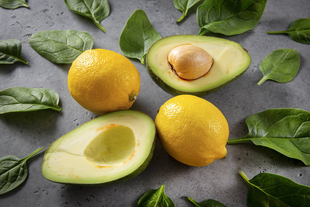 avocado halves with a stone, whole lemons, fresh green spinach leaves on a gray background - Фото, изображение