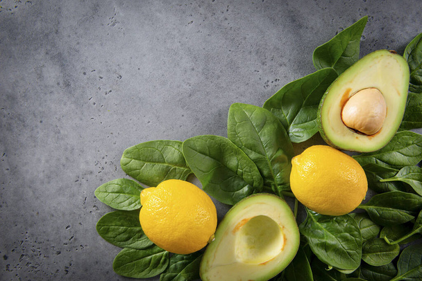 avocado halves with a stone, whole lemons, fresh green spinach leaves on a gray background, flat lay,  copy space,  - Foto, Bild