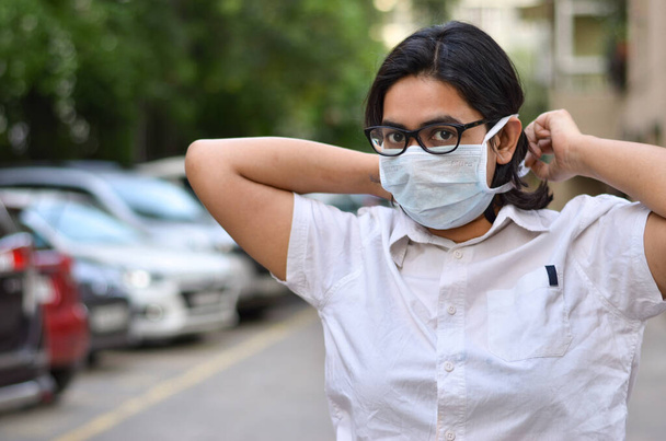 Портрет молодої медичної допомоги жінка-працівниця, яка зв'язує хірургічну маску на обличчі, щоб захистити себе від корони Вірус (COVID-19) пандемії на затуманеному тлі - Фото, зображення
