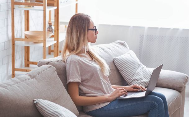 ノートパソコンを持つ女の子はソファに座って仕事 - 写真・画像