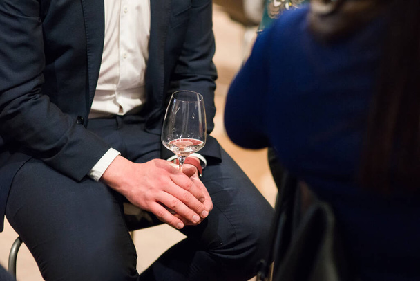 Man in suite sitting holding a glass of white wine, partially photographed on a wine tasting event. - Photo, Image