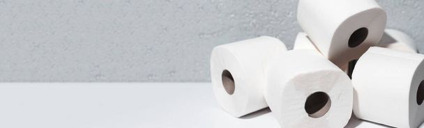 Panoráma banner fénymásoló, közelkép WC papír tekercsek fehér asztalon, háttér texturált fal szürke színű. - Fotó, kép