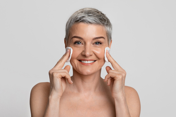 Schöne Frau mittleren Alters reinigt die Haut im Gesicht mit Wattepads - Foto, Bild