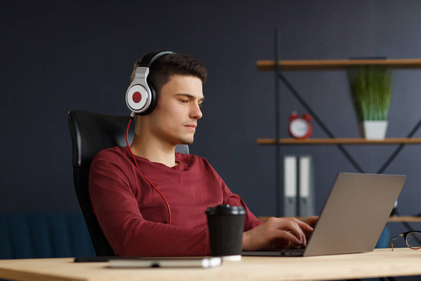 Young freelancer working in home office with laptop and listenin - Zdjęcie, obraz