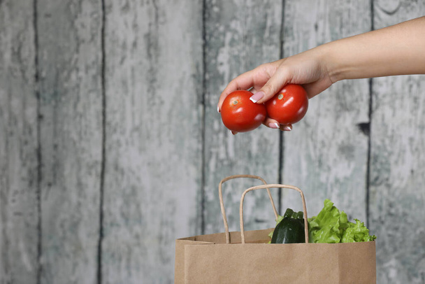 Mujer mano sosteniendo tomate rojo con barra de papel de reciclaje sobre un fondo de madera
 - Foto, Imagen
