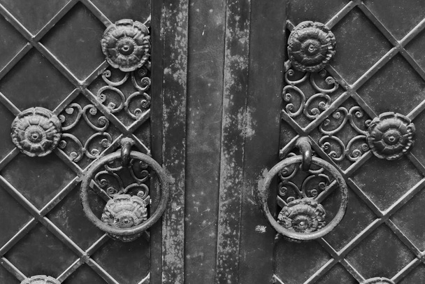 Фрагмент черных чугунных дверей, украшенных цветочным узором с висячими ручками
.  - Фото, изображение