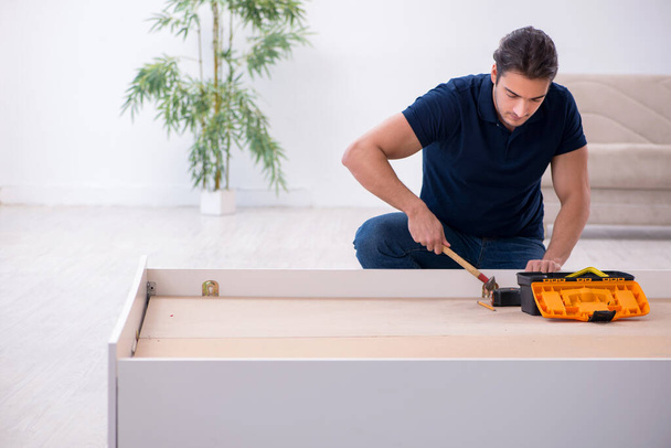 Молодой мужчина-подрядчик устанавливает мебель на дому - Фото, изображение