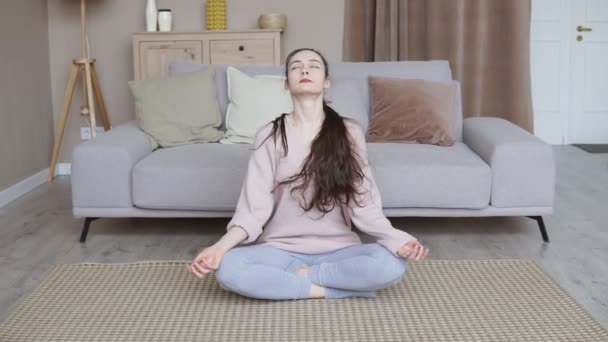Młoda dziewczyna medytująca w domu. Młoda kobieta siedząca na podłodze, aktywny tryb życia, harmonia i koncepcja jogi - Materiał filmowy, wideo