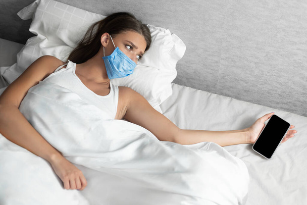 Beteg lány nyúl a Smartphone feküdt az ágyban otthon - Fotó, kép