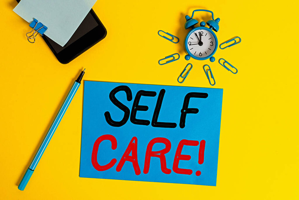 Text sign showing Self Care. Conceptual photo practice of taking action preserve or improve ones own health Smartphone clock clips paper sheet notepad ballpoint colored background. - Photo, Image