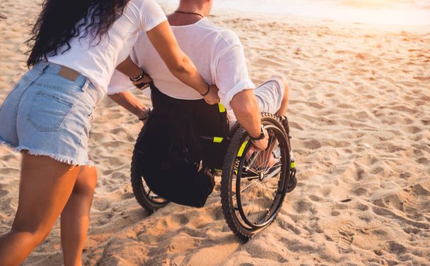 Disabled man in a wheelchair with his wife on the beach. - Zdjęcie, obraz