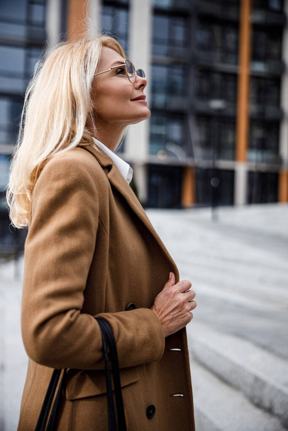 Dreamy blonde lady in eyeglasses standing outdoors - Fotografie, Obrázek