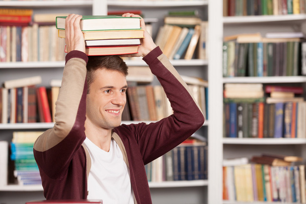 Cheerful young man holding a book stack on his head - Фото, изображение