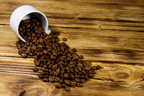 Жареные кофейные зерна проливаются из чашки на деревянный стол - Фото, изображение