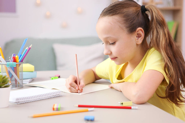 Cute little girl is doing homework in the interior of the room. - 写真・画像