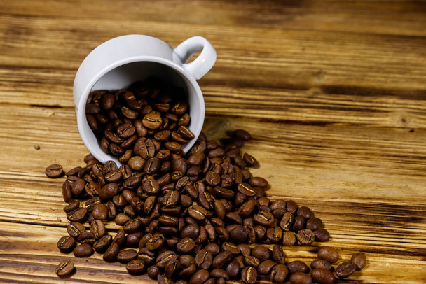 Жареные кофейные зерна проливаются из чашки на деревянный стол - Фото, изображение