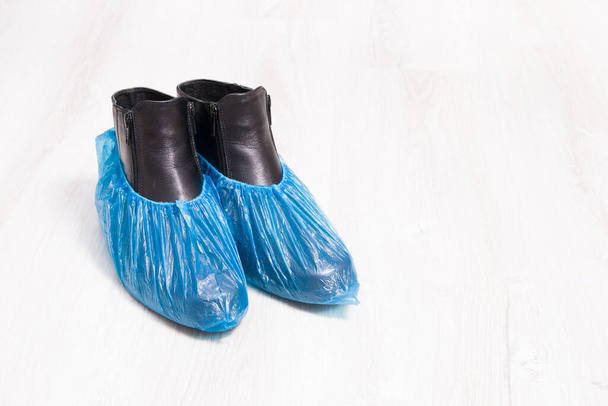 black leather boots in blue disposable shoe covers on a wooden light floor copy spac - Zdjęcie, obraz