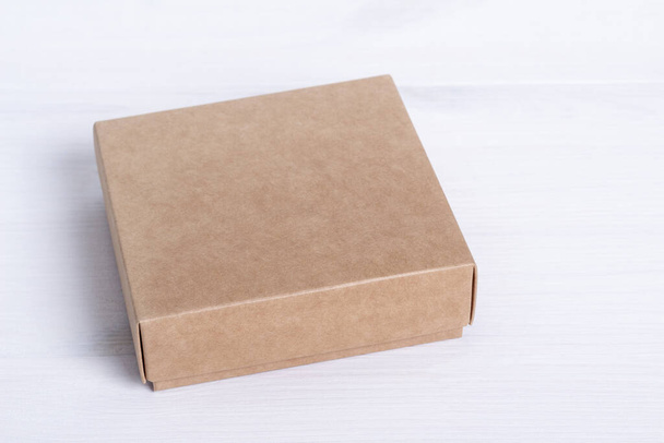 Pacchetto scatola di cartone bianco isolato su sfondo di legno bianco. Artigianato scatola di carta vista laterale. Cartone piccolo quadrato chiuso. Spedizione pacchetto eco. Pacchetto di consegna. Idea regalo, eco-lifestyle. Concetto naturale
. - Foto, immagini
