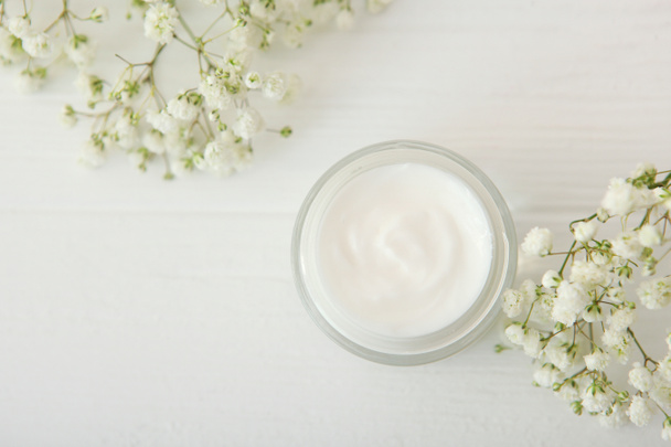 Care crème en bloemen op een gekleurde achtergrond bovenaanzicht. Schoonheidsmiddelen voor huidverzorging. - Foto, afbeelding