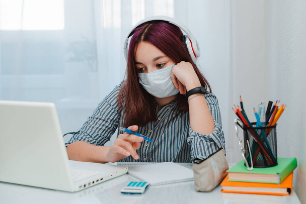teen schoolgirl with medical mask against viruses sitting floor living room sofa student studying home laptop doing homework - Photo, Image