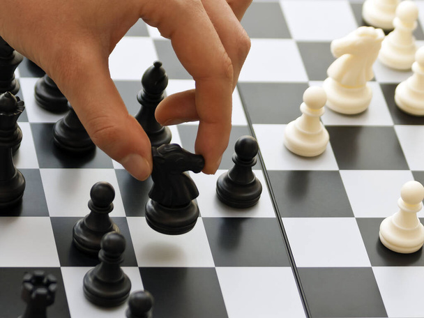 Close-up of a left hand moving a black knight on a chessboard  - Foto, imagen