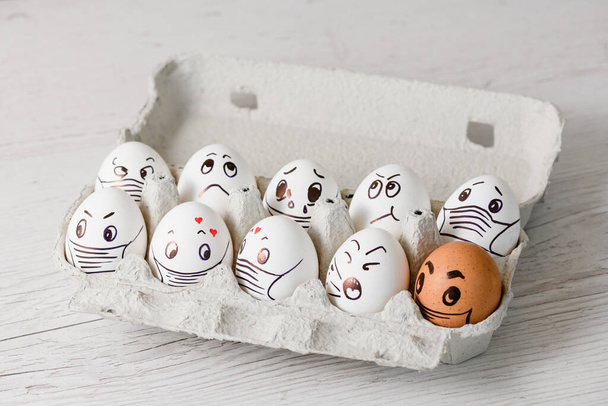 Különböző érzelmű húsvéti tojásokra rajzolt vicces arcok - bánat, boldogság, meglepetés, járvány, sírás papírtálcán a koronavírus karantén elszigetelésére szolgáló maszkban - Fotó, kép