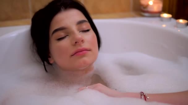 Young beauty brunette girl relaxing in hot babble bathroom, self-care, cozy home - Materiał filmowy, wideo