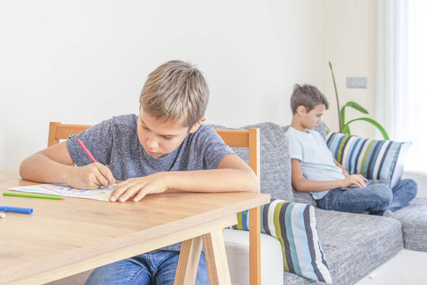 Education, online learning, distance learning, entertiment at home. Boy drawing with colored pencils. Brother using laptop computer for homework, watching video, playing games - 写真・画像