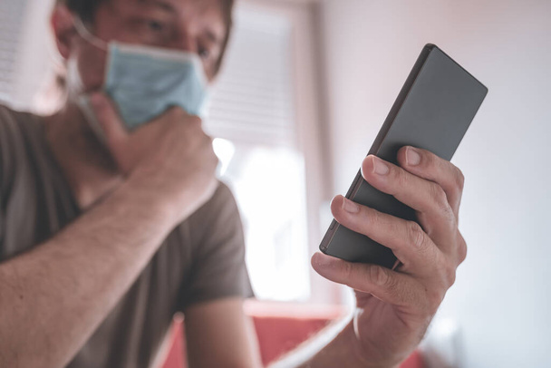 Worried man using mobile phone in home quarantine self-isolation for having Covid-19 coronavirus symptoms, selective focus - 写真・画像