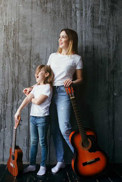 Beautiful mother and daughter learn to play the guitar during the quarantine and isolation - Foto, afbeelding
