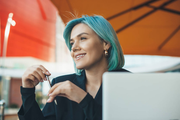 Γοητευτική επιχειρηματίας με μπλε μαλλιά κάθεται σε ένα εστιατόριο και εργάζεται με έναν υπολογιστή - Φωτογραφία, εικόνα