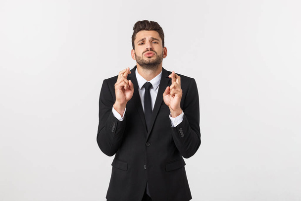 Businessman fingers cross on copy space. Handsome young man in suit looking at camera while standing against white background. - Foto, afbeelding