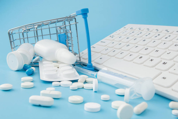 Shopping cart toy with medicaments and Keyboard. Pills, blister packs, medical bottles, thermometer, protective mask on a blue background. . Health care and internet shopping. Top view with place for your text. - Foto, Imagen