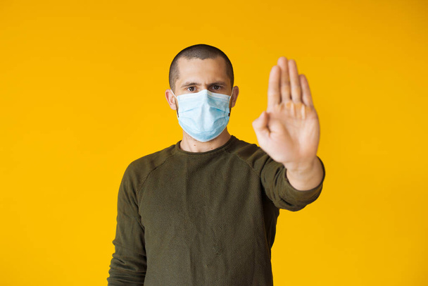 Hombre caucásico con el pelo corto posando en una pared amarilla es gesto parada mientras usa una máscara blanca especial
 - Foto, imagen