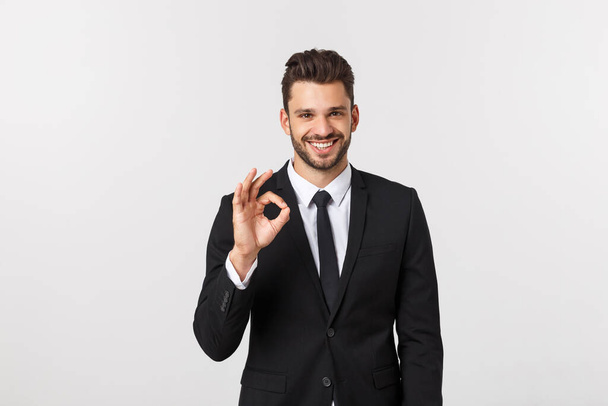 Knappe glimlachende zakenman toont ok teken met vingers over grijze achtergrond. - Foto, afbeelding