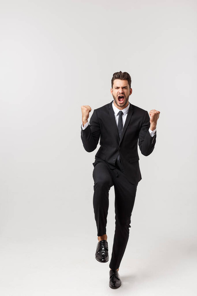 Cheerful young bearded business man show hand up excited with clenched fists. Full length portrait business man isolated over white studio background - Fotoğraf, Görsel