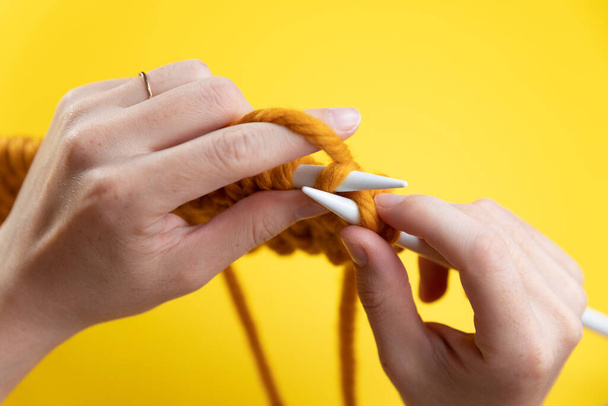 Women's hands knit from yellow wool on a yellow background, top view. Hand knitting - 写真・画像